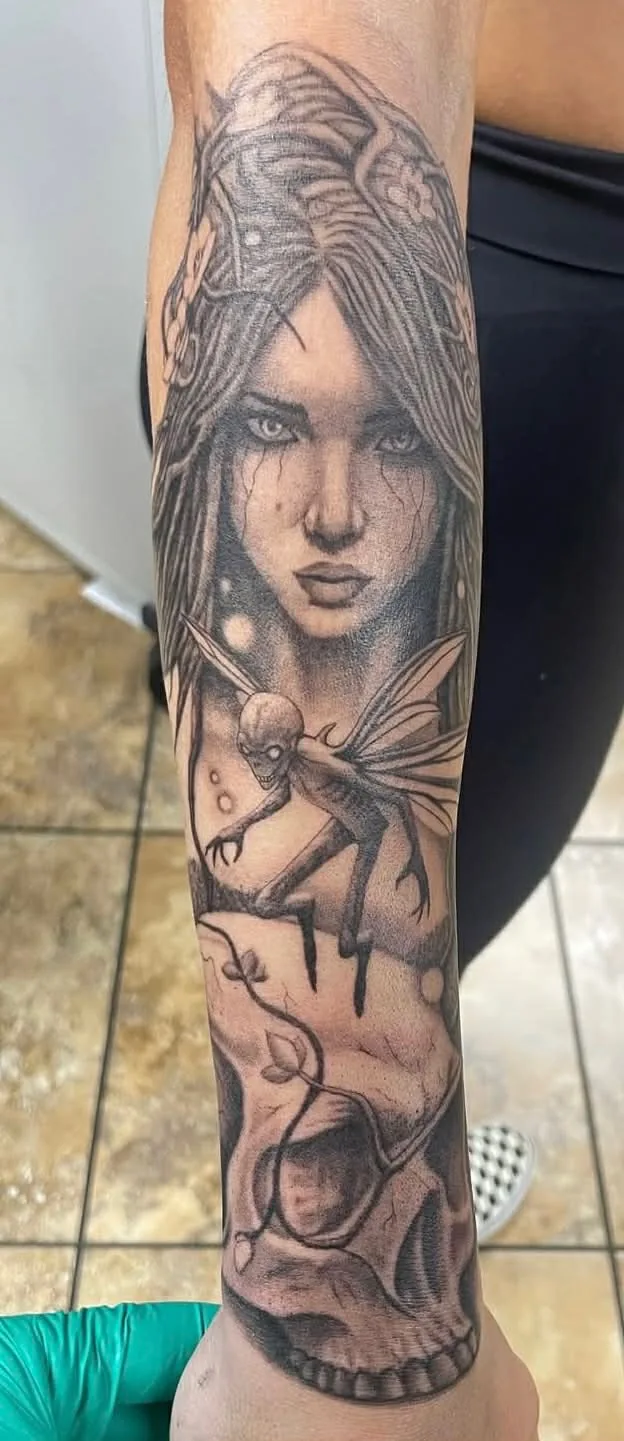 Woman's face, winged creature, and skull tattoo on arm
