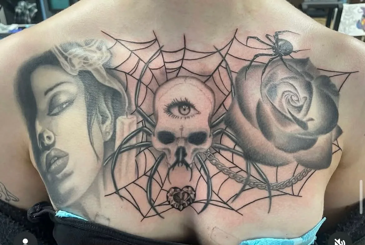 Chest tattoo featuring a woman's face, spider skull, rose, and spider web